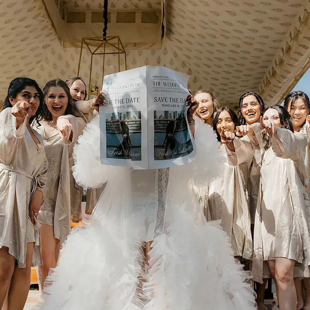 Bride in a white tulle robe reading from the personalised wedding newspaper with bridesmaids in gold robe