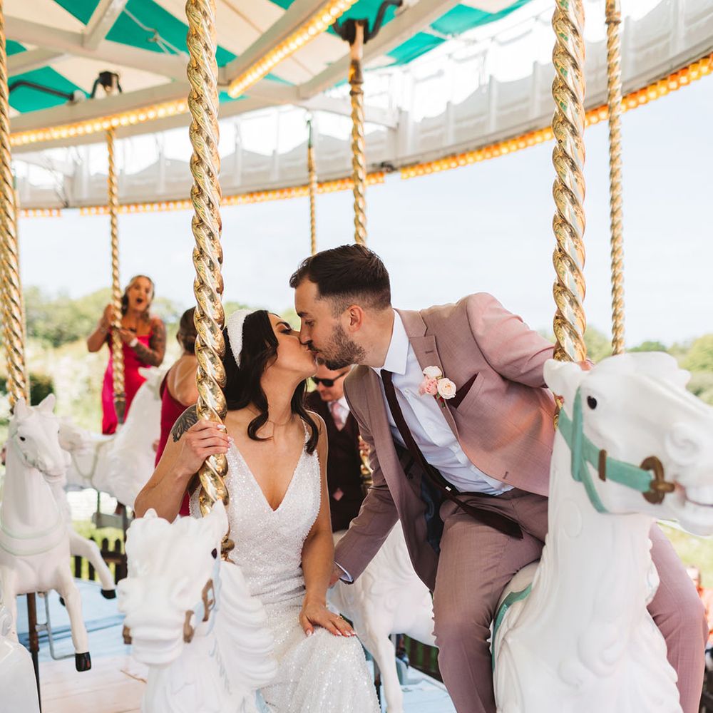 Bride and groom kiss riding on a carousel at Preston Court