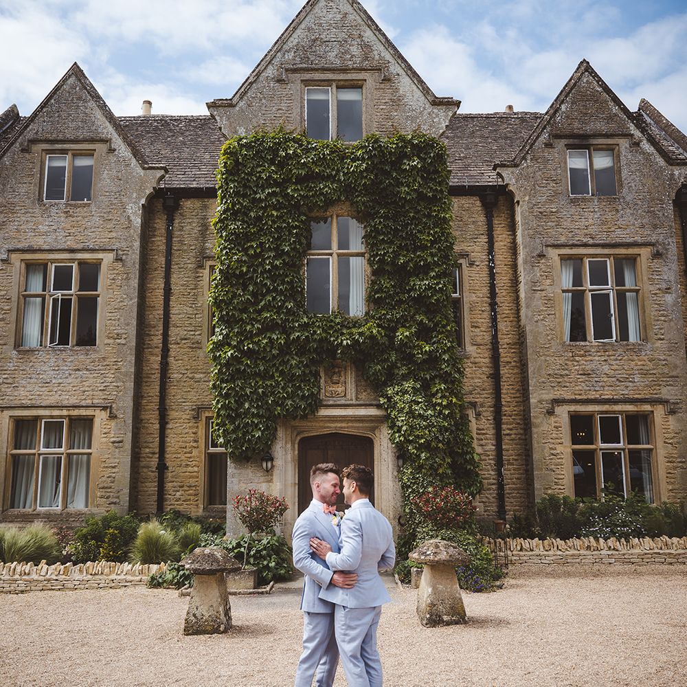 Grooms in matching suits in front of luxe country house
