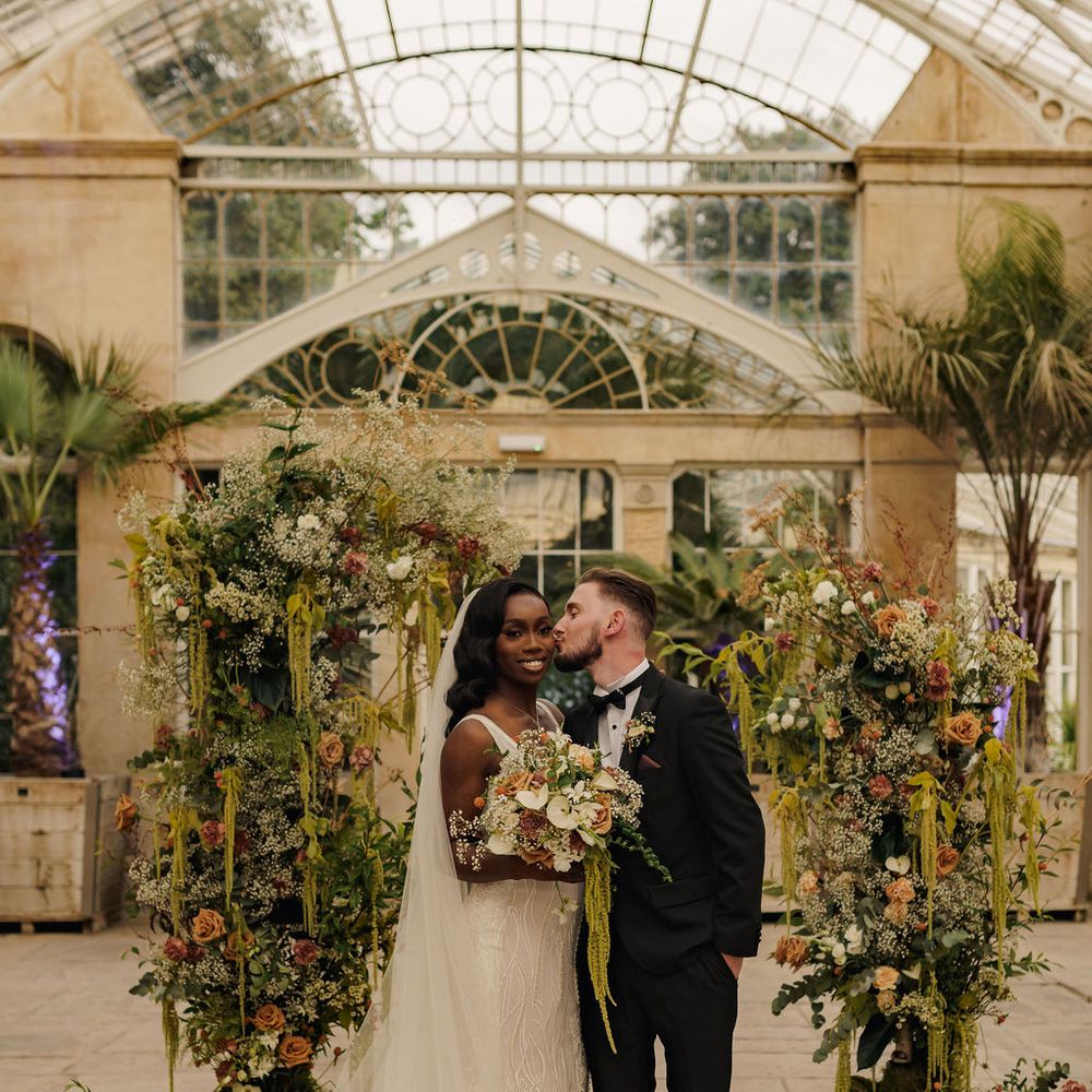 Couple kiss in front of their stunning altar decor at glasshouse wedding venue