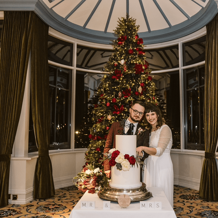 couple-cuts-cake-in-front-of-christmas-tree