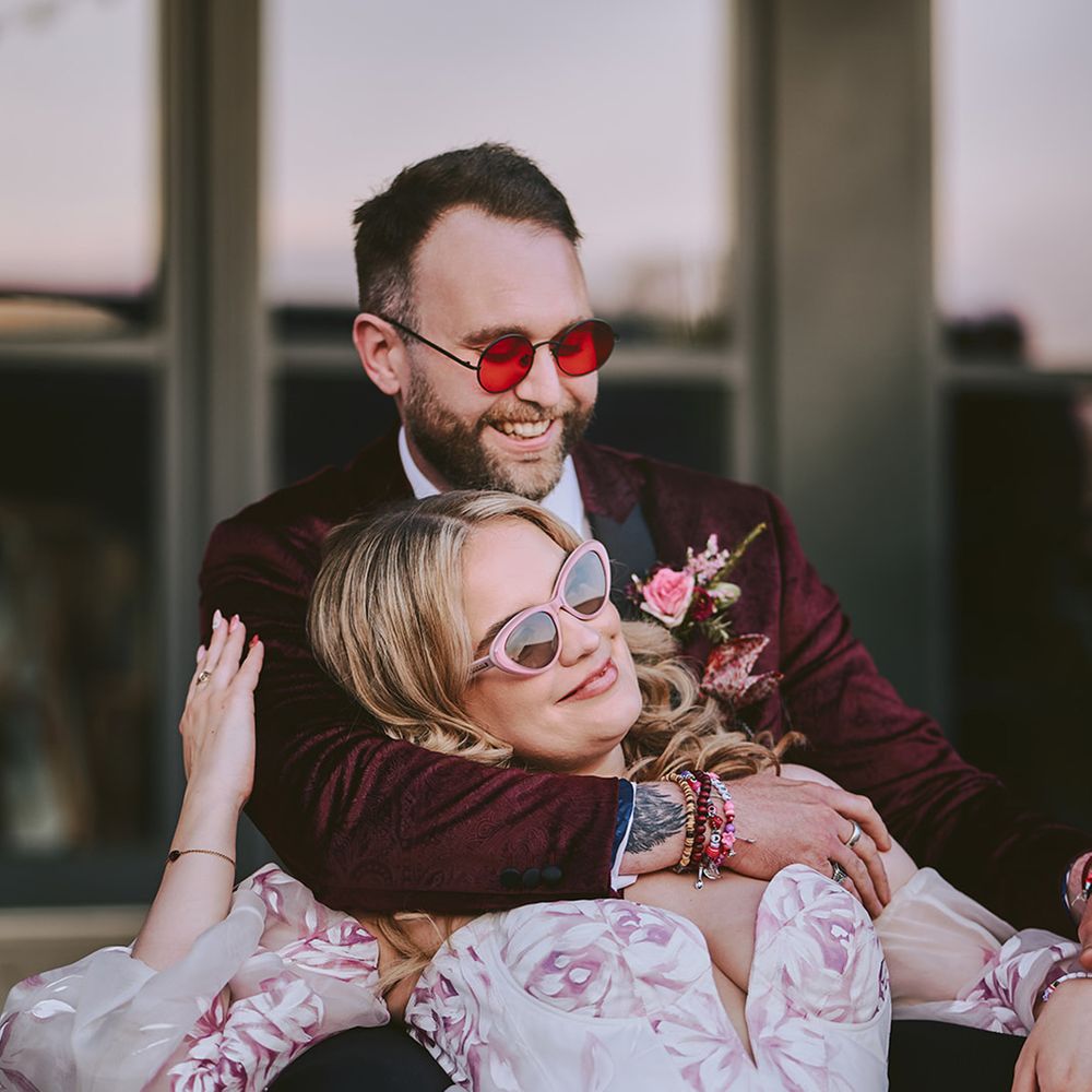 groom-in-red-velvet-suit-embraces-bride-in-pink-floral-wedding-dress