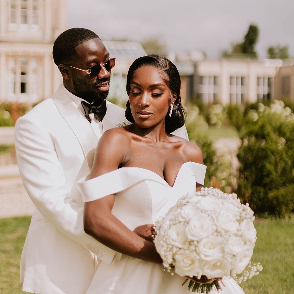 groom-in-white-tuxedo-embraces-bride-in-off-the-shoulder-wedding-dress