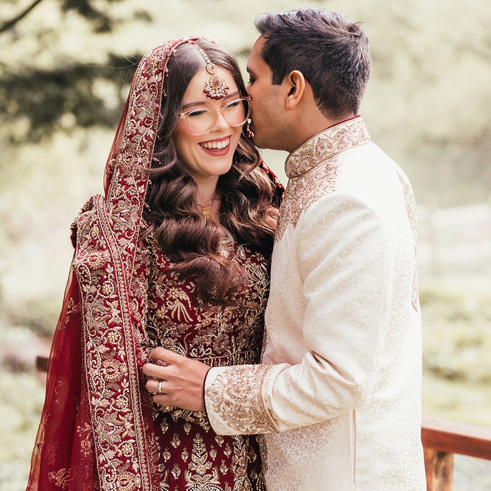 groom-kisses-bride-on-cheek-who-wears-red-gold-lehenga-outfit