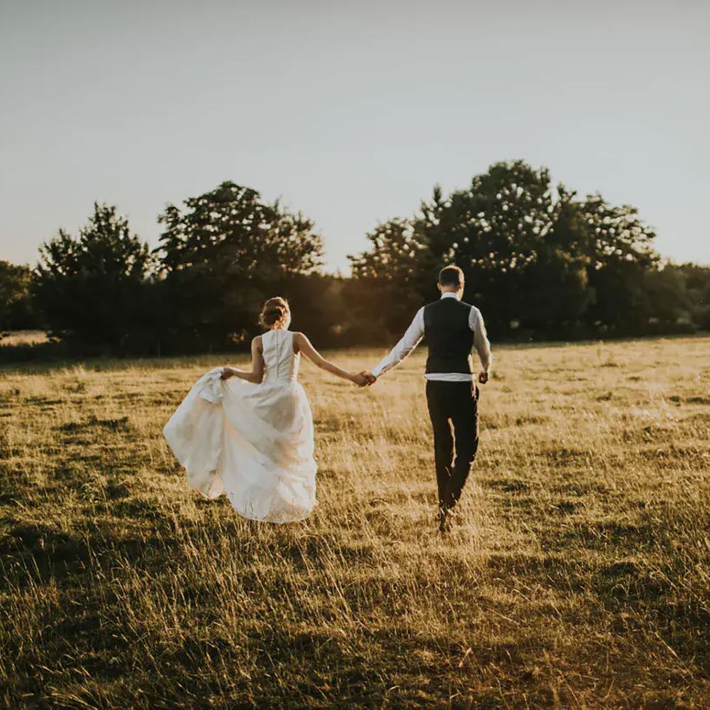Couple walks hand in hand in field at Tythe Barn 
