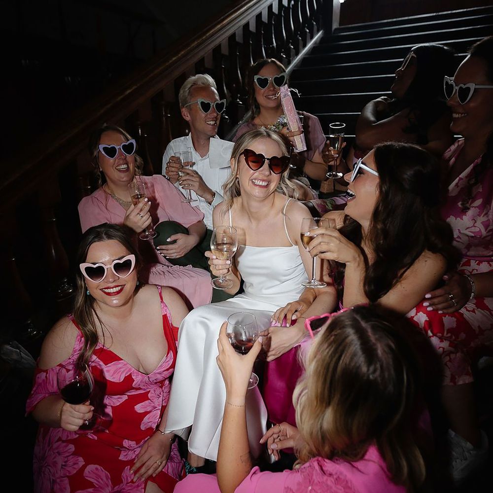 Bride in white satin wedding dress with sunglasses with the bridal party wearing pink bridesmaid dresses