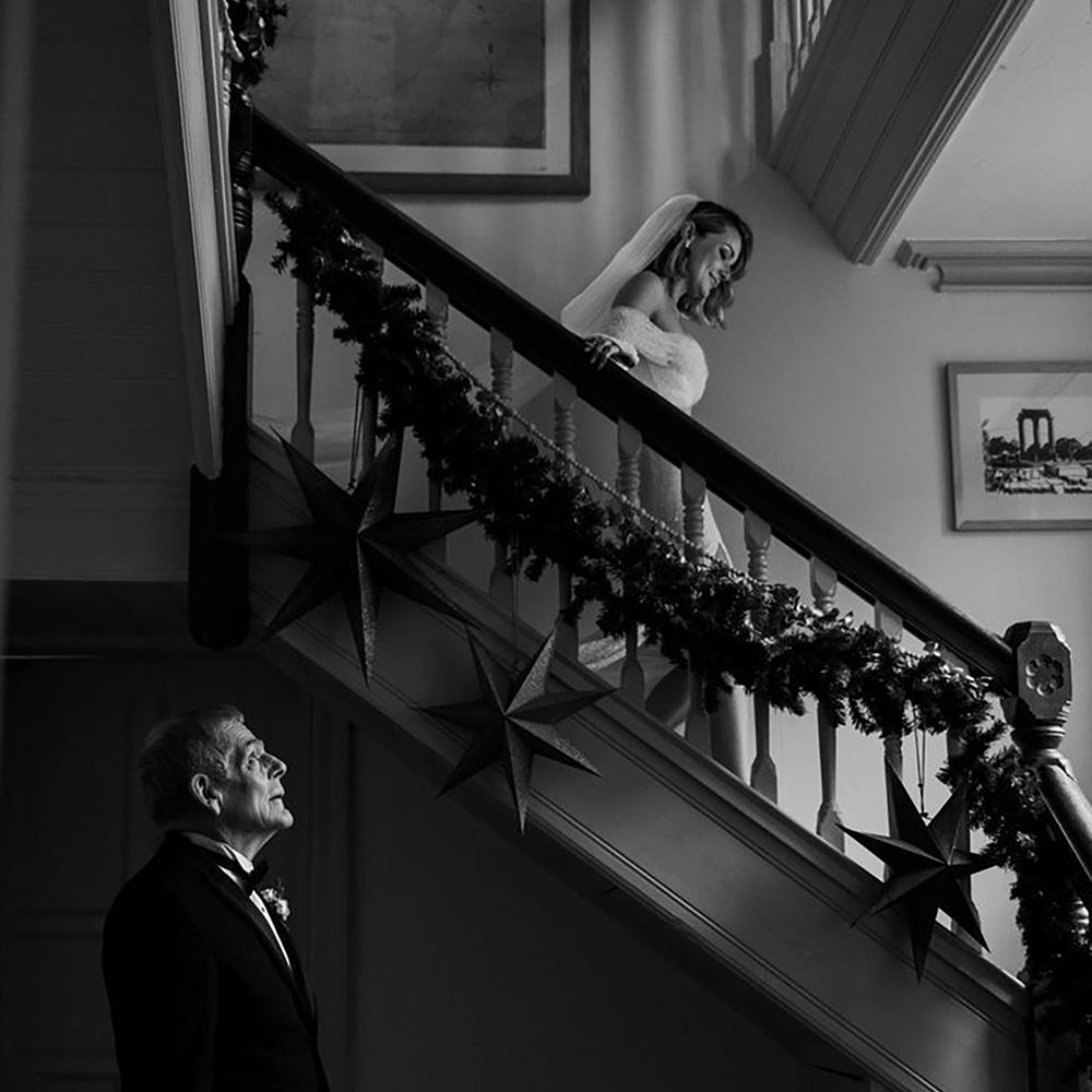 bride walks down the stairs in her wedding dress towards the father of the brid