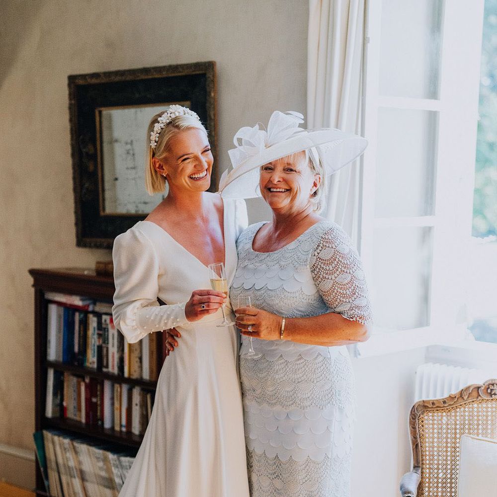 mother of bride wearing light blue dress and hat standing with bride