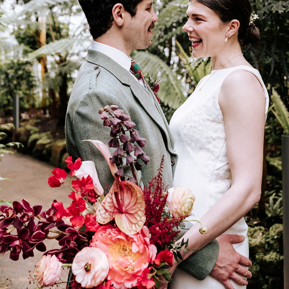 groom-in-green-suit-jacket-embraces-bride-in-bespoke-wedding-dress