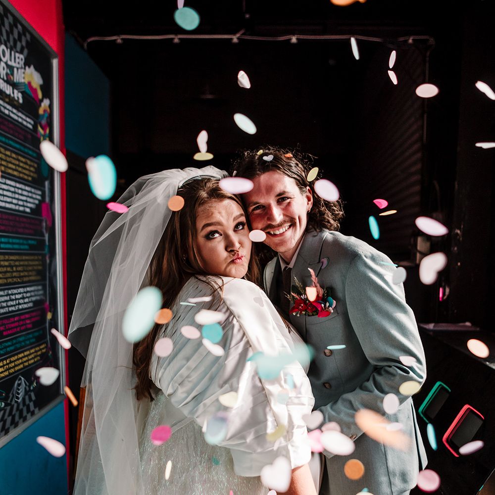 bride-and-grooom-embrace-as-pastel-retro-confetti-flies-around-them