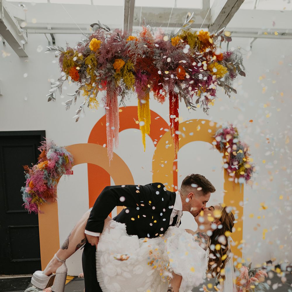 bride-in-platform-heels-swooped-in-kiss-in-front-of-neon-backdrop-arches