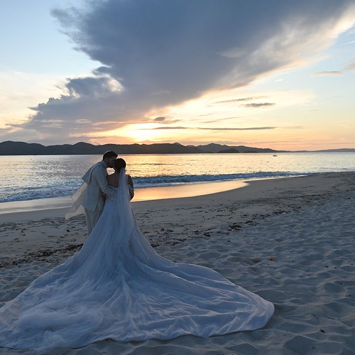 Bride wearing twenty three foot veil embracing groom on the beach