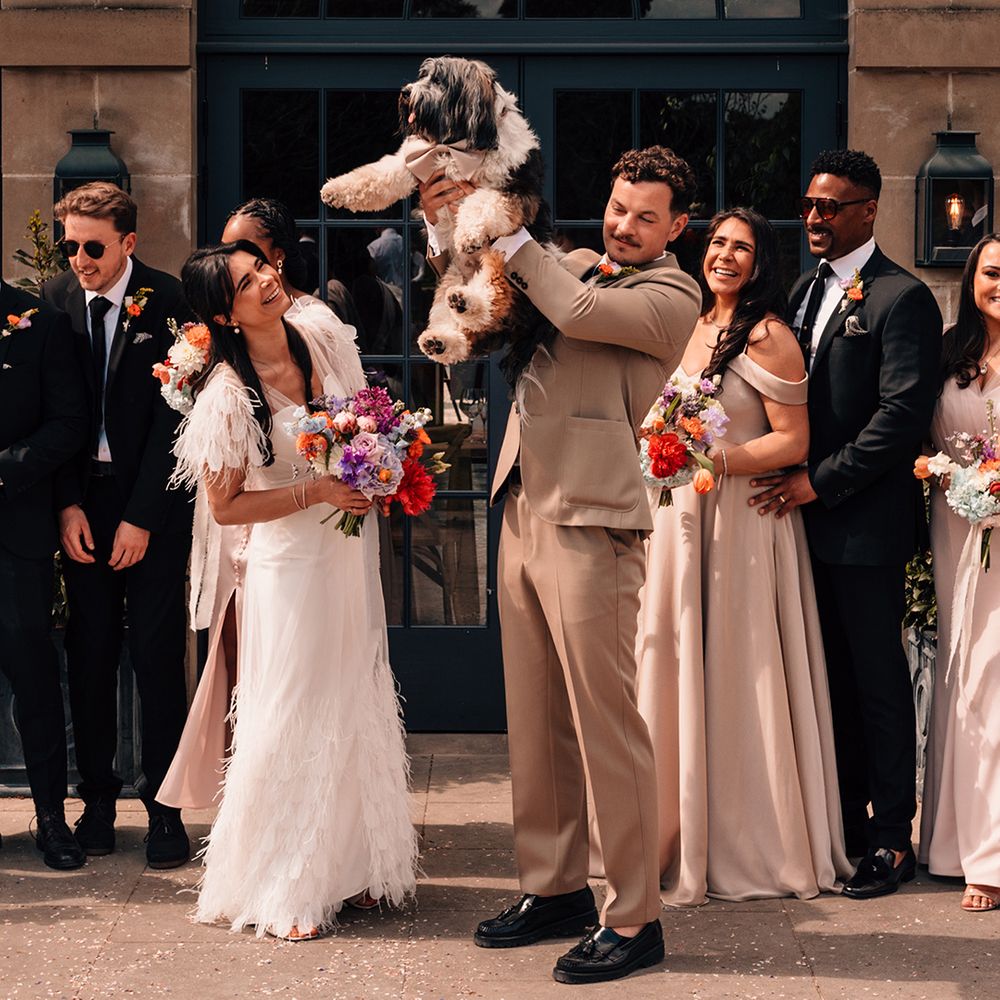 Wedding party celebrates as the groom lifts his pet dog in the air