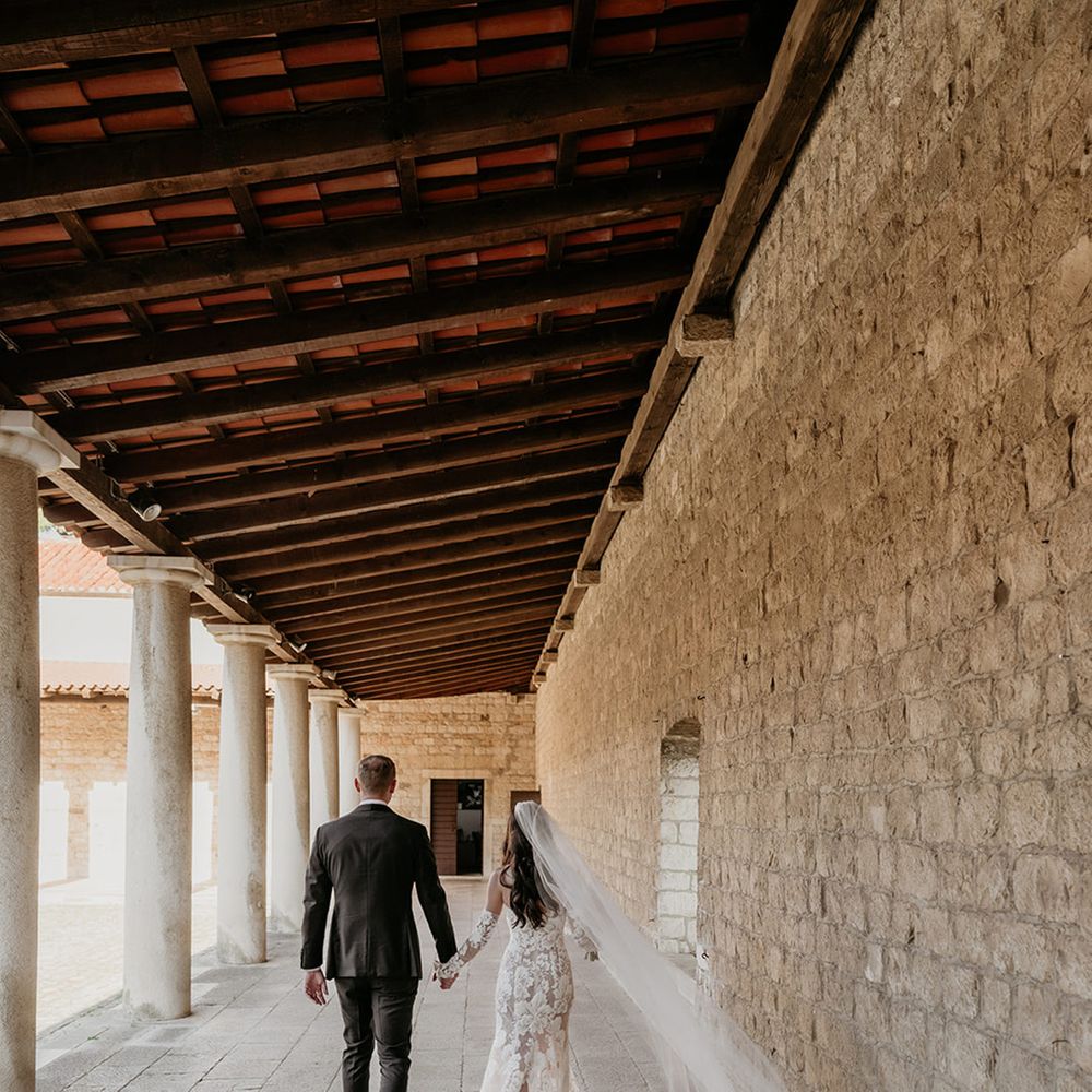 groom-in-black-tuxedo-walking-with-bride-in-floral-wedding-dress-with-long-veil