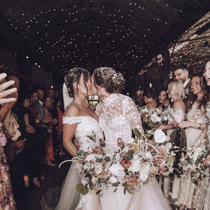 Two Brides in Flower Wedding Dresses Kissing During Confetti Moment