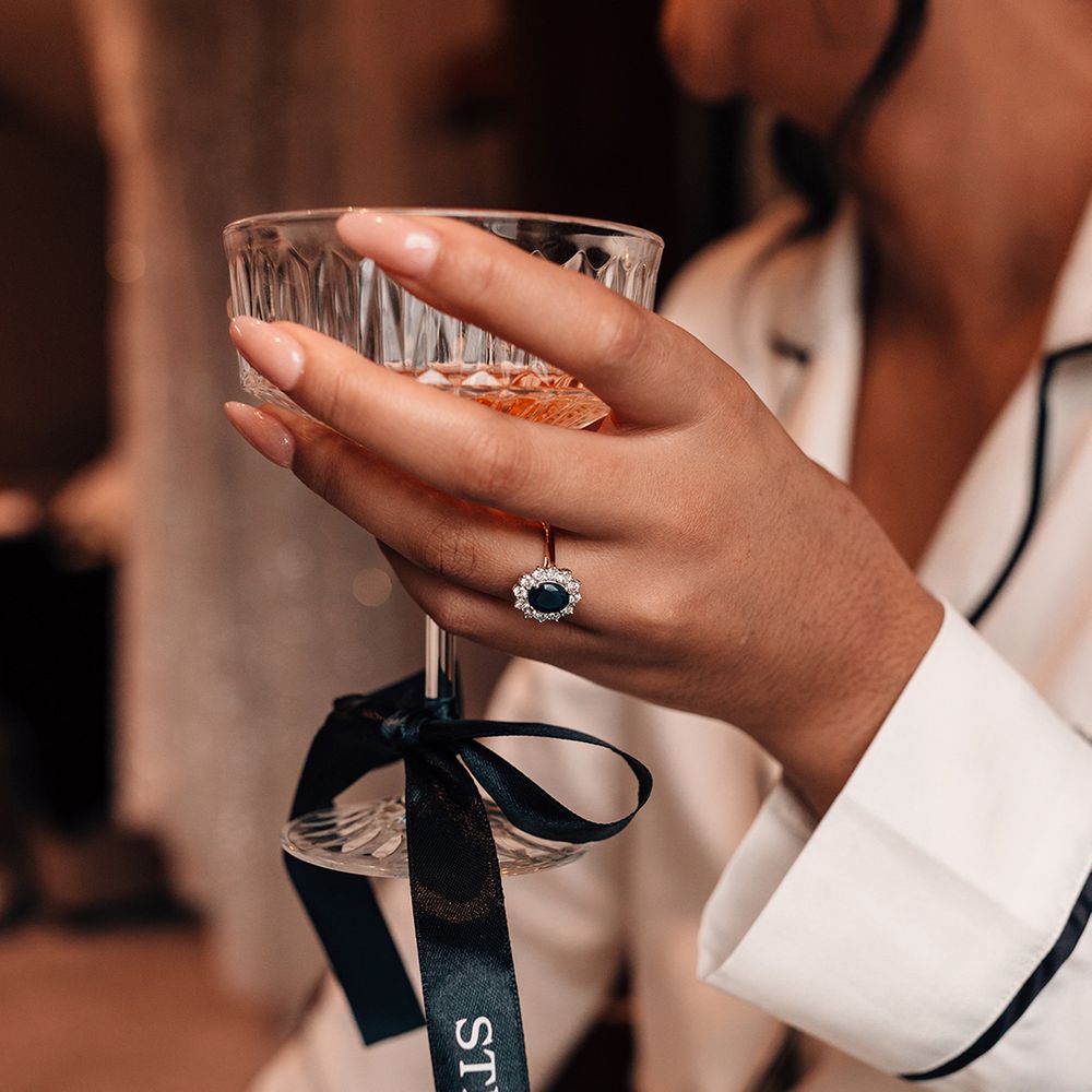 bride-wearing-sapphire-halo-engagement-ring-holding-champagne-glass-with-personalised-bow