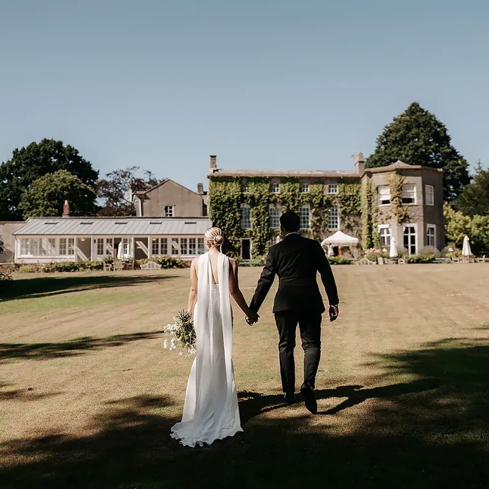 Pennard House sustainable wedding venue, couple holding hands on lawn
