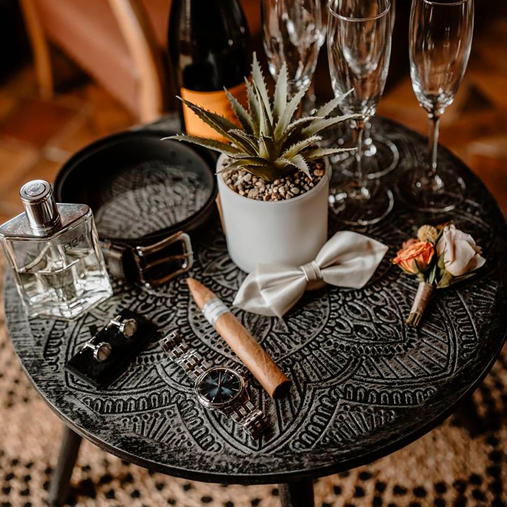 Table of groom's accessories including grey bow tie, floral buttonhole, cigar, silver watch and silver cufflinks