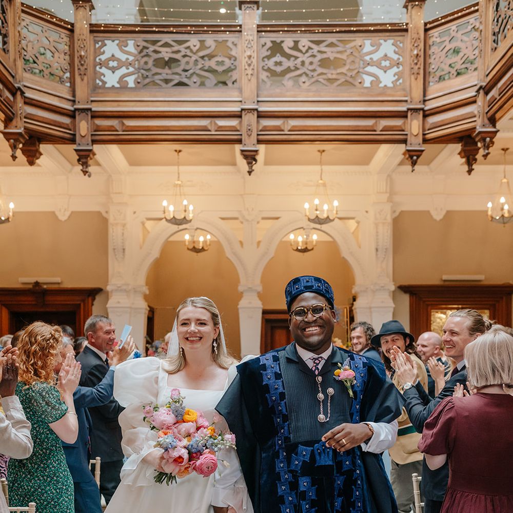groom-in-dark-blue-agbada-with-bride-in-mesh-puff-sleeve-wedding-dress-with-bright-bouquet