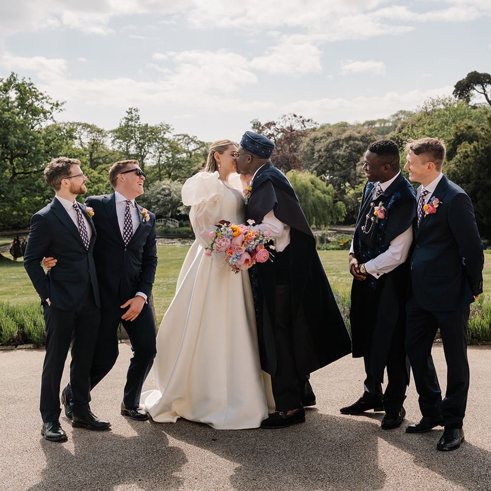 groomsmen-in-navy-suits-with-bride-and-groom-kissing