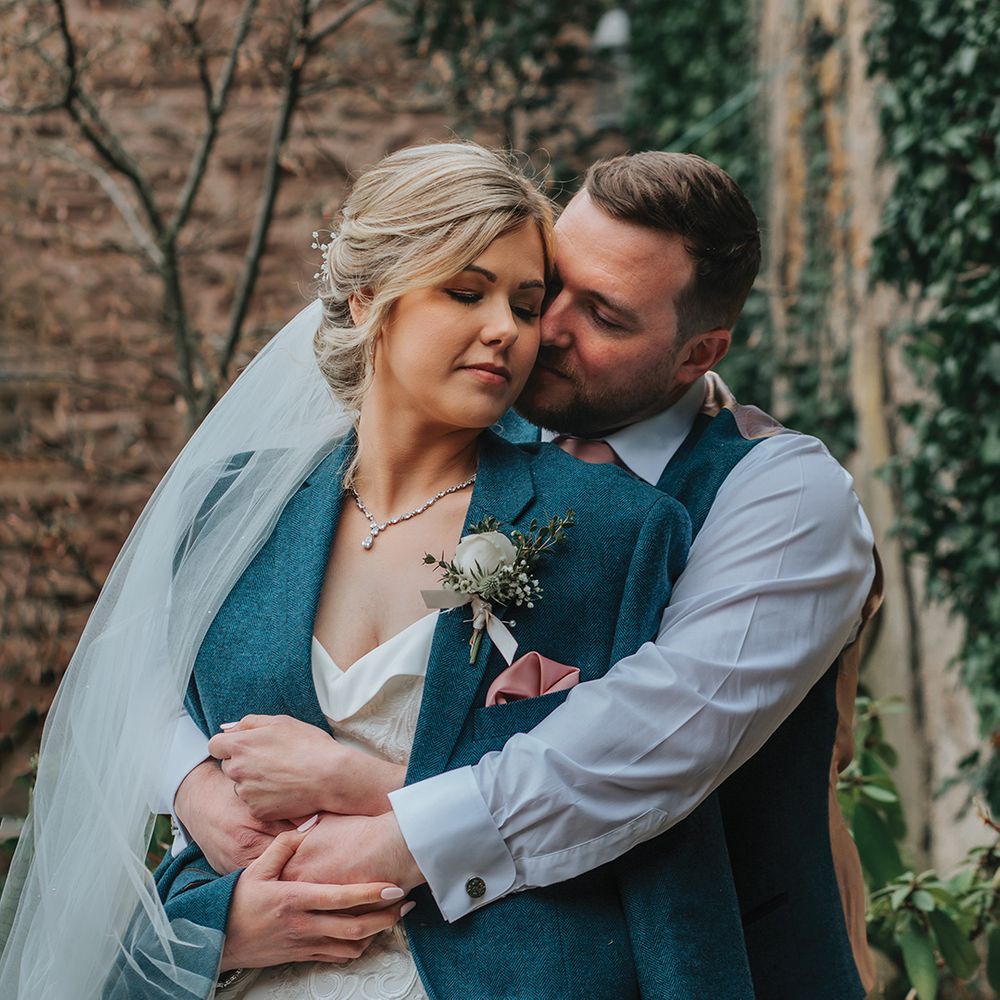 groom-embraces-bride-from-behind-as-she-wears-his-suit-jacket