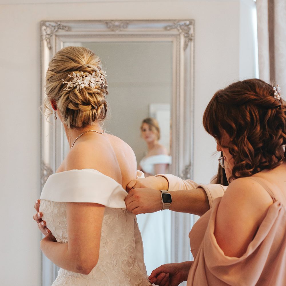 mother-of-the-bride-helps-bride-into-off-the-shoulder-wedding-dress
