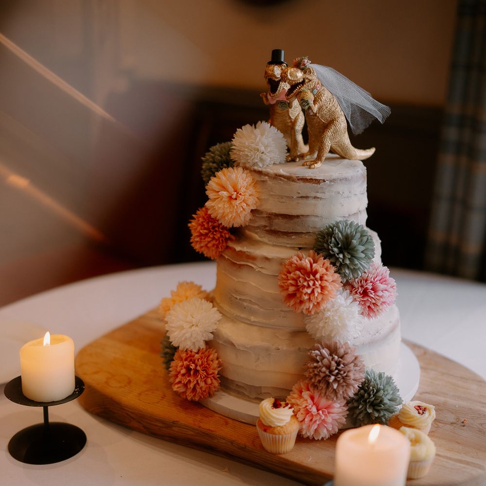 three-tier-semi-naked-wedding-cake-with-dinosaurs-and-pom-poms