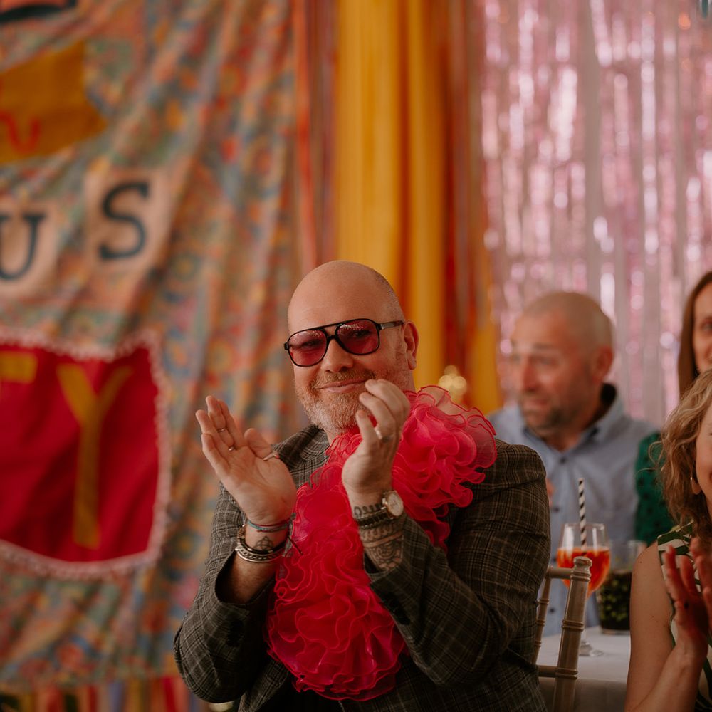 wedding-guest-in-sunglasses-and-pink-lapel-claps