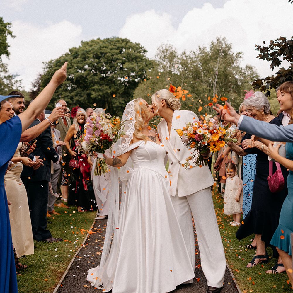 bride-in-drop-waist-wedding-dress-and-bride-in-white-suit-share-a-kiss