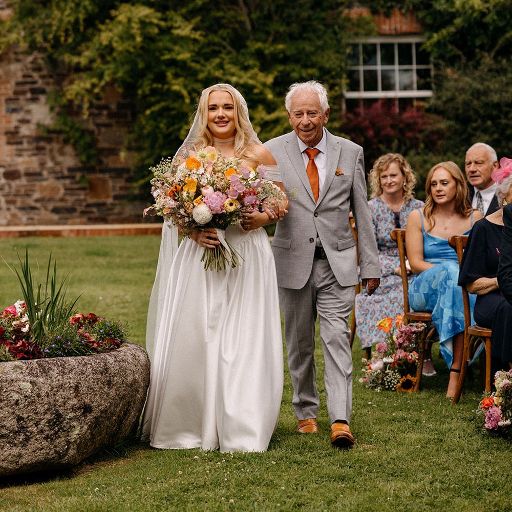 father-of-the-bride-in-grey-suit-walks-bride-down-the-aisle-at-outdoor-wedding