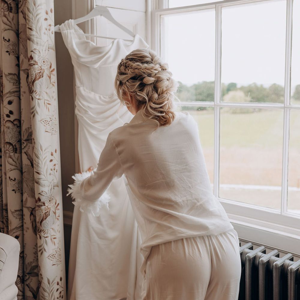 bride-in-white-pyjamas-looks-at-wedding-dress