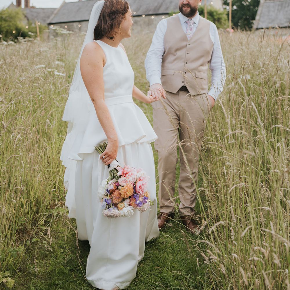 peplum-wedding-dress-for-bride-walking-with-groom-in-beige-waistcoat