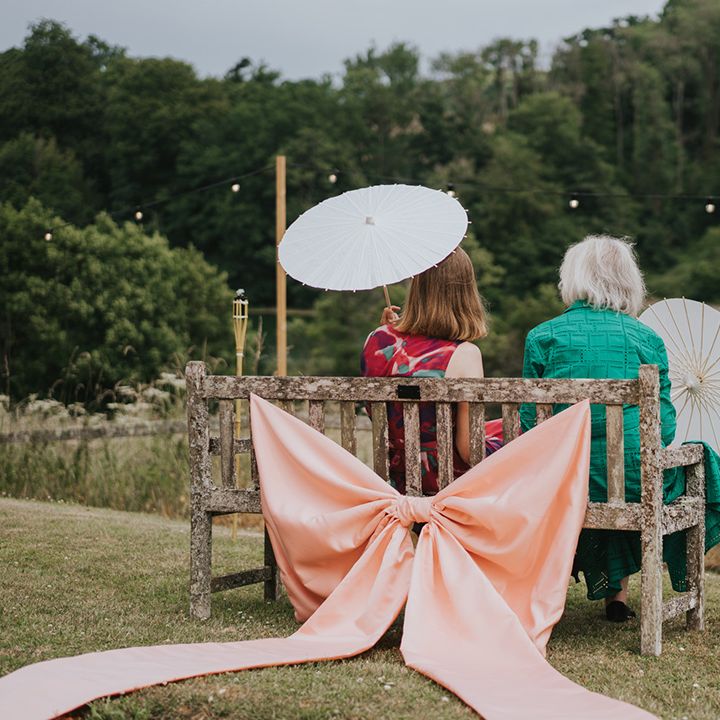 wedding-guests-seated-on-wooden-bench-with-pink-bow-decor