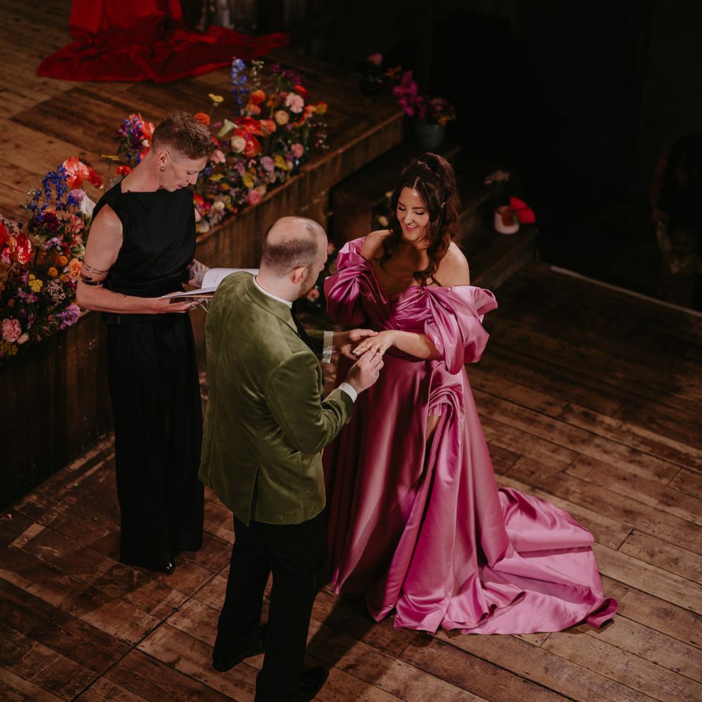 groom-in-green-velvet-suit-jacket-holds-hands-with-bride-in-pink-wedding-dress-exchanging-vows