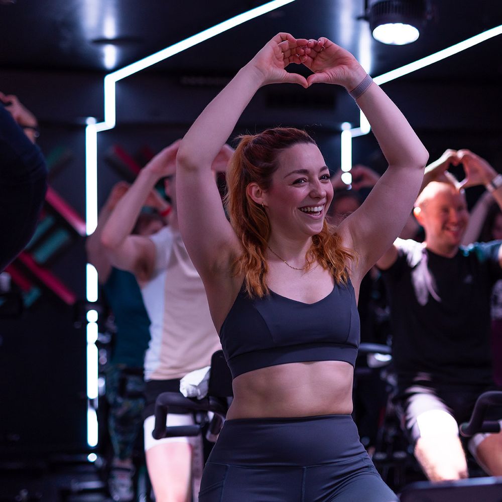 People doing heart hands in Digme Fitness spin cycle wellness class