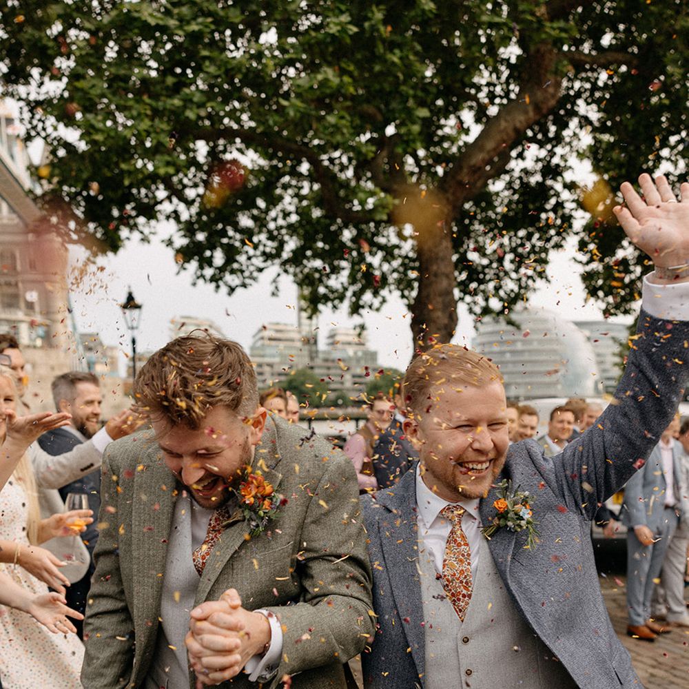 Two grooms smile as their guests throw confetti over the couple
