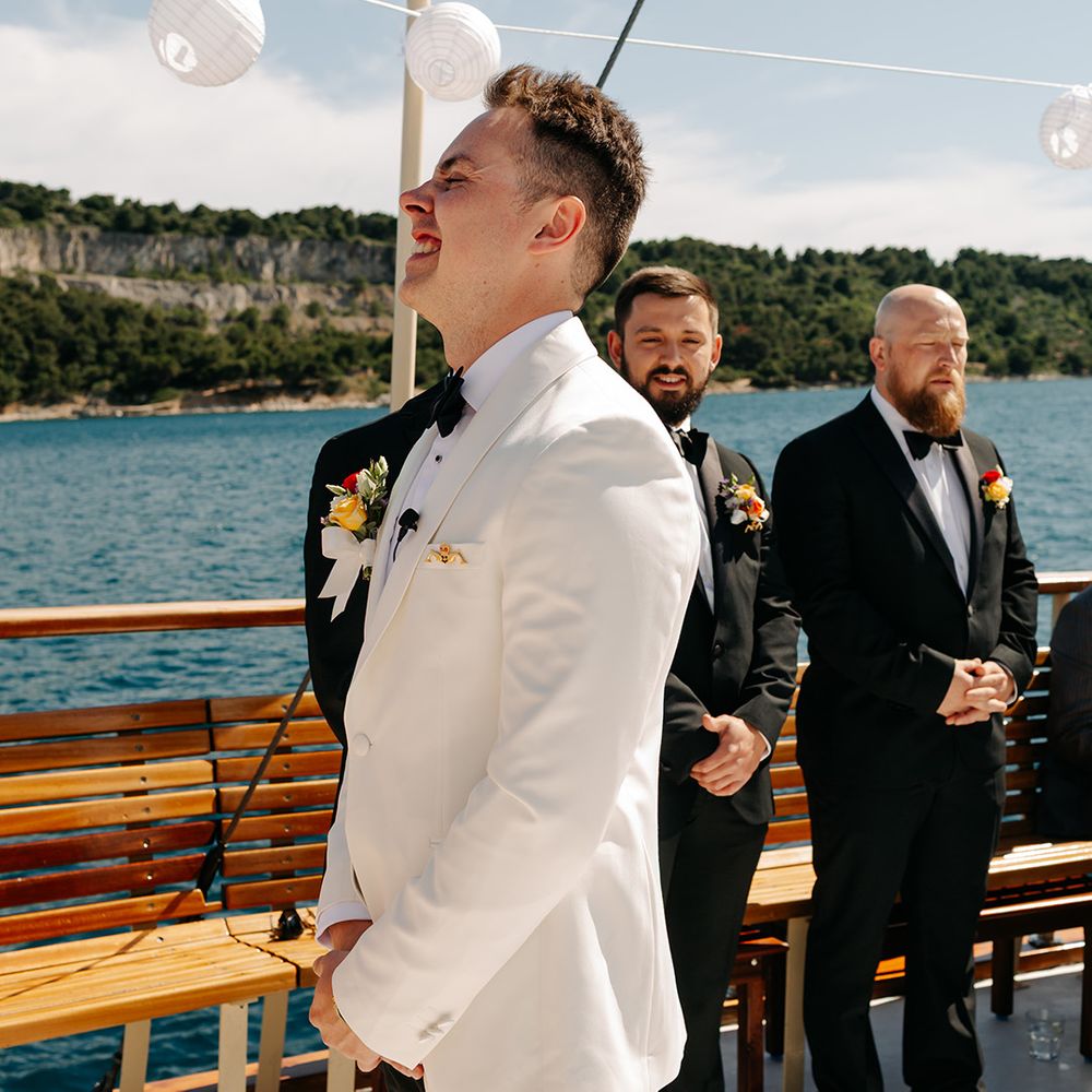 Groom waits eagerly in white tuxedo for first look at bride 