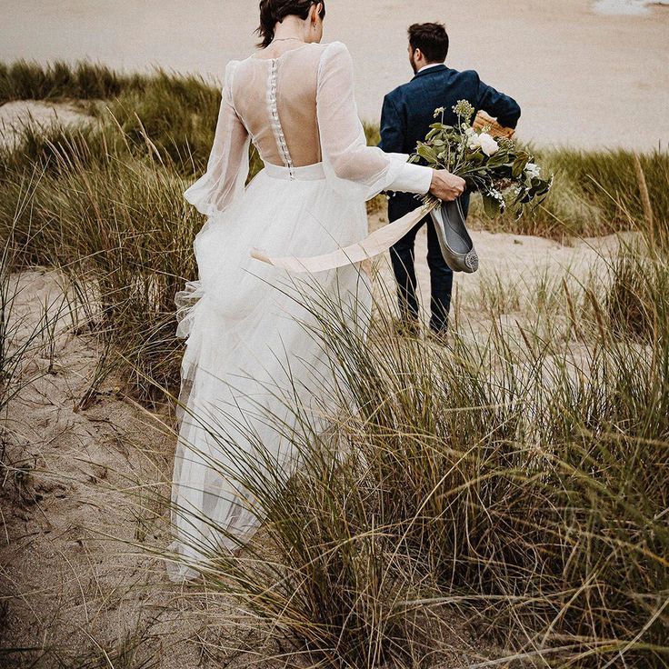Bride in Sheer Back Sassi Holford Wedding Dress with Groom Walking on Beach in Cornwall For Wedding