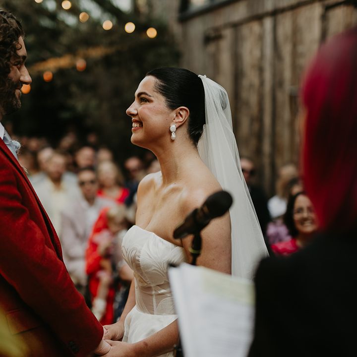groom-in-colourful-red-wedding-suit-smiling-at-bride-during-ceremony