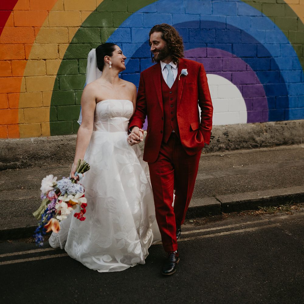 groom-in-red-suit-and-bride-in-strapless-floral-wedding-dress-with-rainbow-pattern-south-london-backdrop