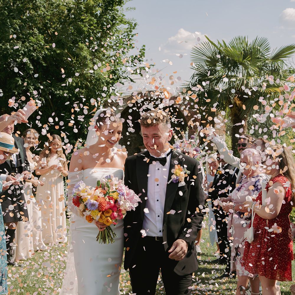 groom-in-black-tux-walks-with-bride-through-confetti