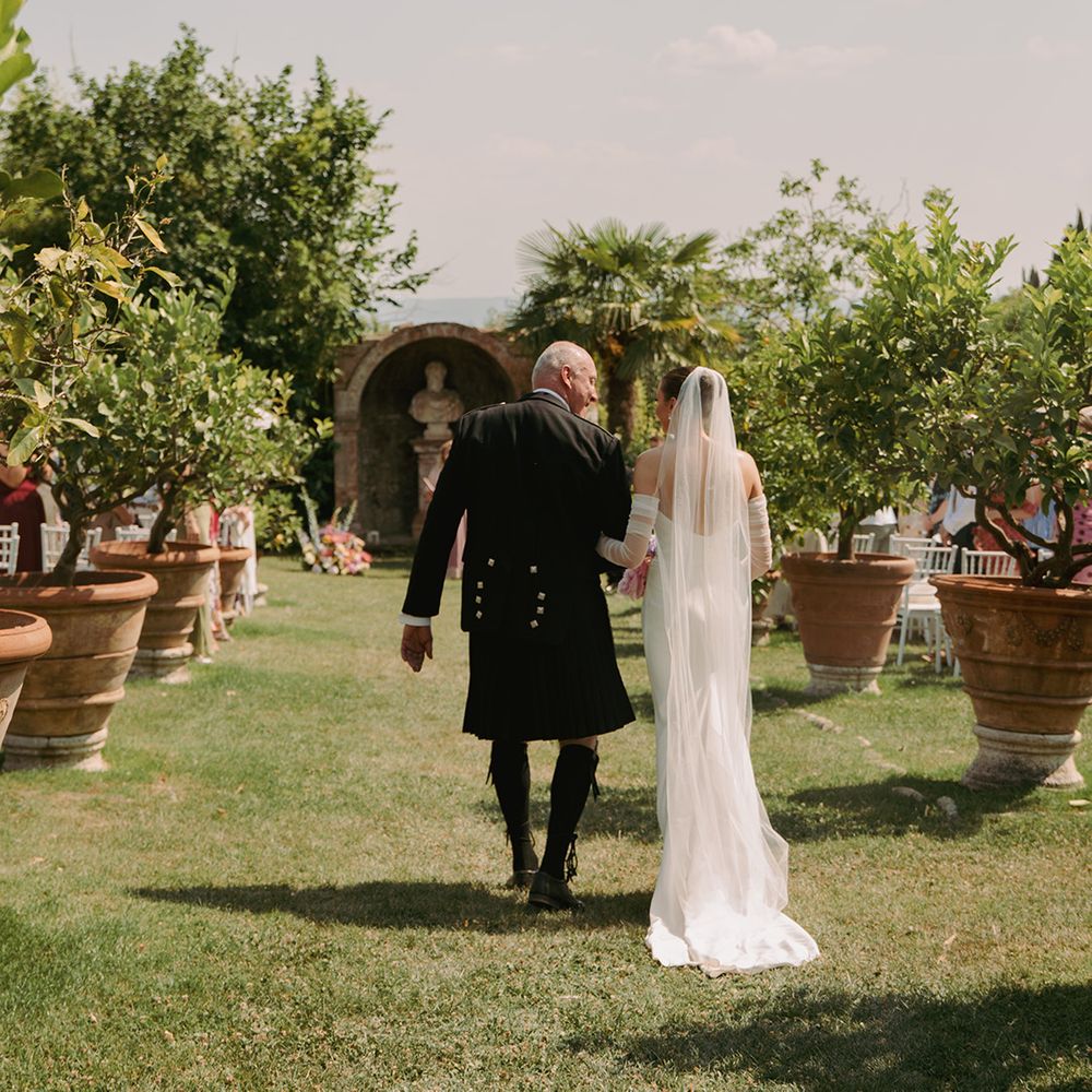 olive-trees-marking-wedding-aisle-as-bride-walks-with-father-of-the-bride