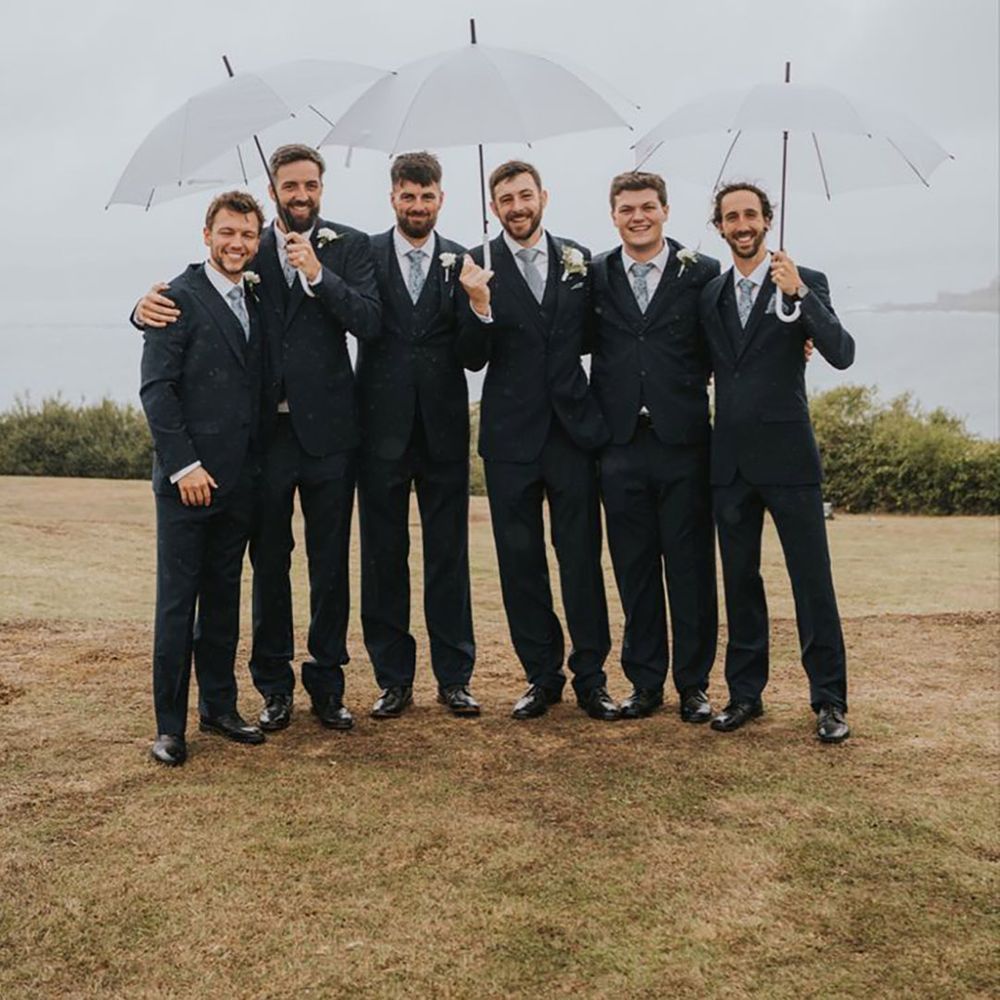 Groomsmen holding clear umbrellas at rainy wedding