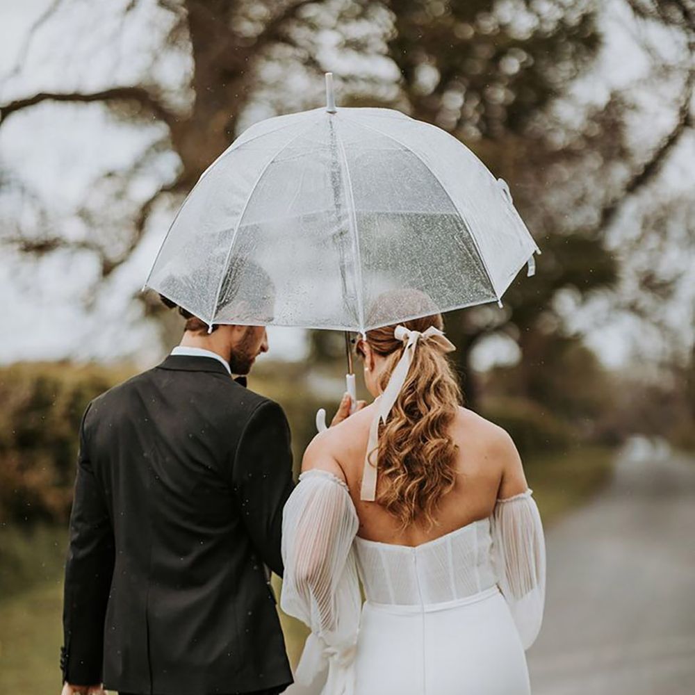 Groom holds clear umbrella for the couple to walk under on rainy wedding day