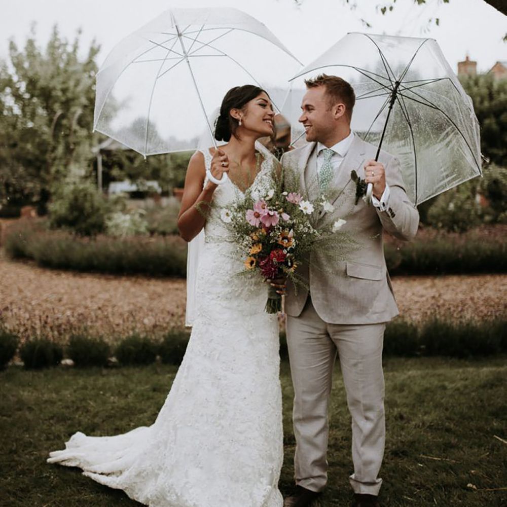 Bride and groom smiling at each other holding clear umbrellas