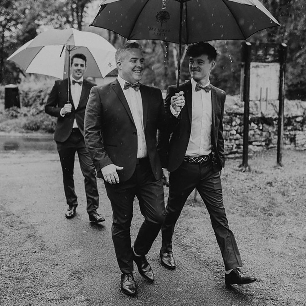 Groomsmen walking together under umbrella walking to the wedding