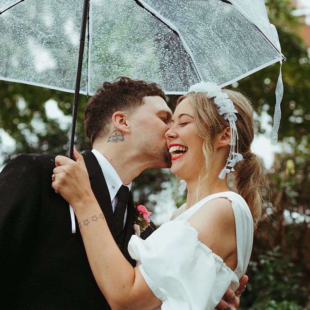 Groom kisses the bride's cheek under clear umbrella