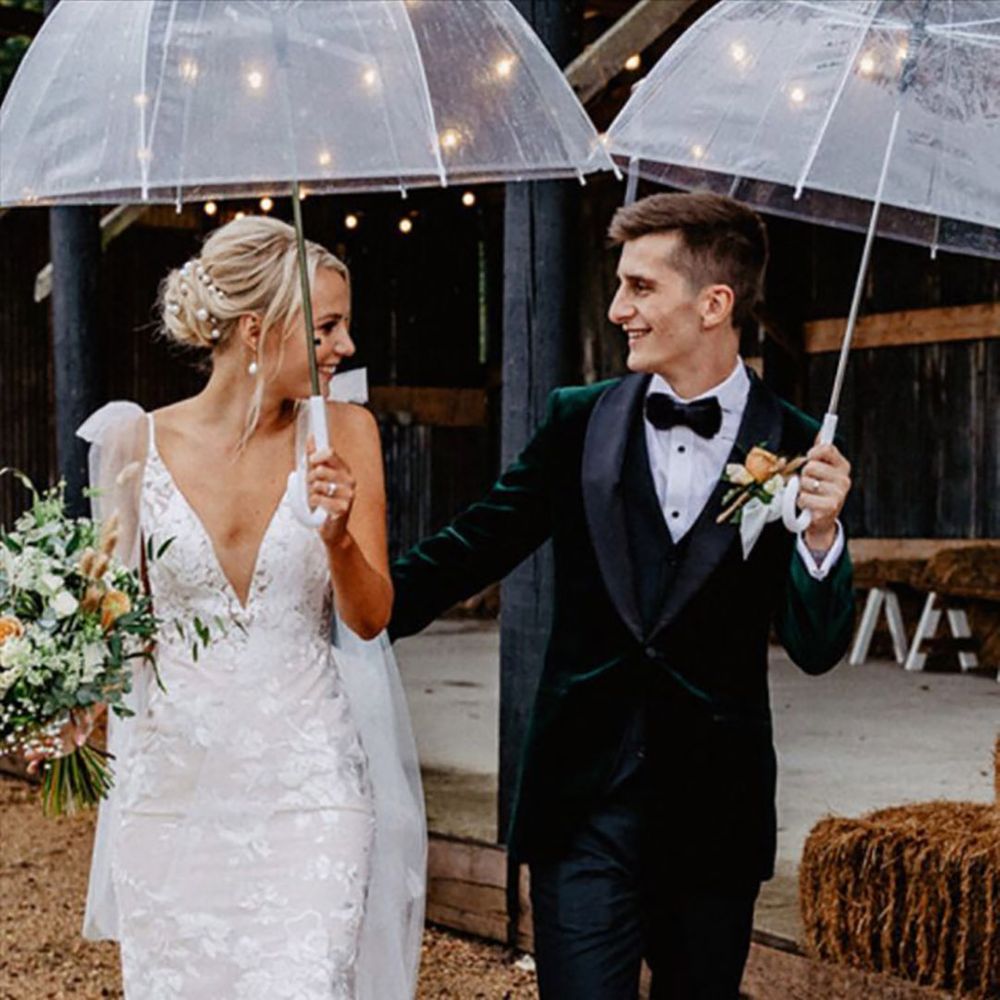 Bride and groom walking together under clear umbrella at black tie wedding