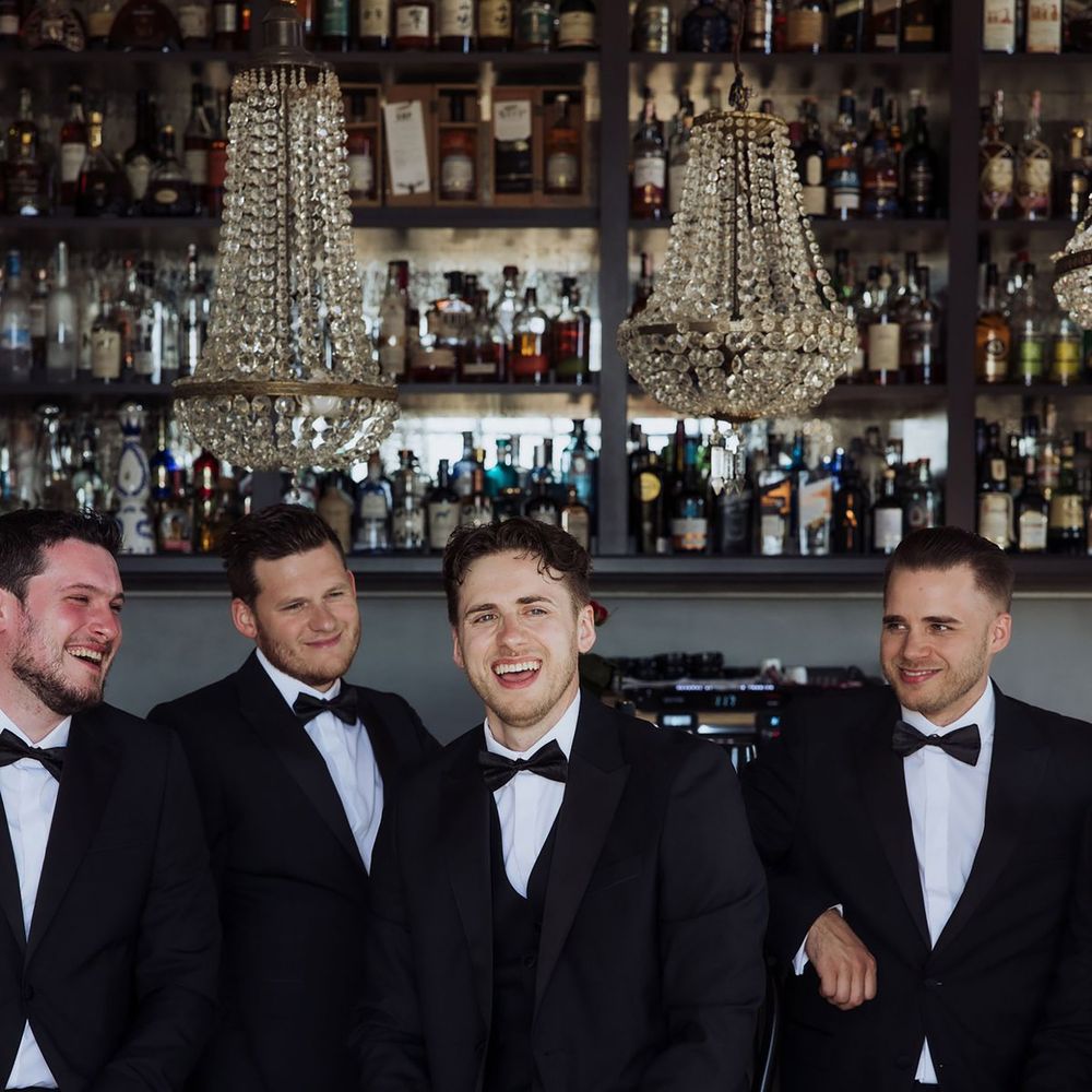 Groom and groomsmen pose for group photos at the bar in tuxedos