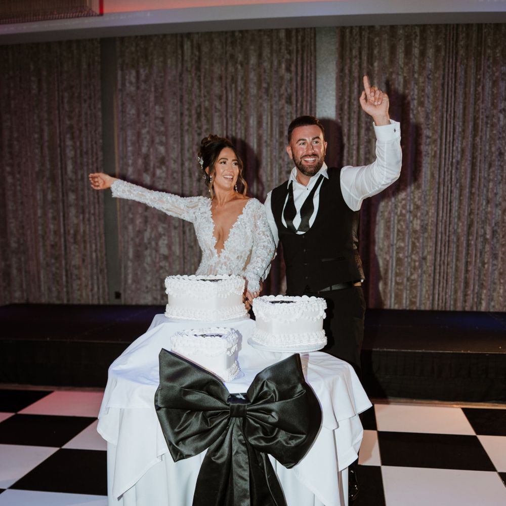 couple-cuts-cake-on-checkered-dance-floor-with-large-black-bow-decor